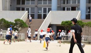 監視員(右)の指示で、「半地下」と呼ばれる場所へ避難する児童ら=7日午前11時27分、宜野湾市新城・普天間第二小学校
