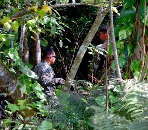 訓練場内の茂みの中で、落下したタイヤを探す米軍関係者ら=9日午後1時すぎ、金武町