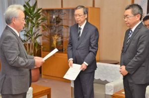 中嶋浩一郎沖縄防衛局長(右)、川田司外務省沖縄大使(中央)に抗議文を手渡す富川盛武副知事=8日午後、沖縄県庁