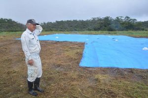 米軍ヘリが炎上した現場を訪れた地権者の西銘晃さん。事故機があった場所はブルーシートで覆われ、足元の牧草は踏み倒されて茶色に変色していた=21日午前11時25分、東村高江