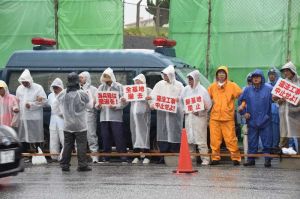 雨の中、工事車両の進入を防ぐため工事車両用ゲート前でスクラムを組む市民ら=30日午前8時40分