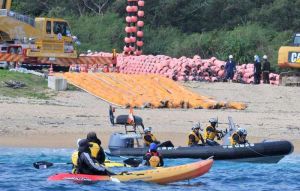 フロートをクレーン車でつり上げて砂浜に並べる作業に、抗議する市民ら(手前)=4日午前11時34分、名護市辺野古のキャンプ・シュワブ(下地広也撮影)