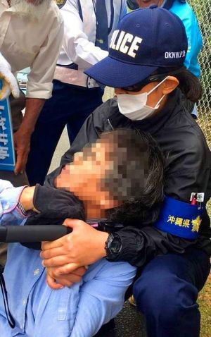 警察官に押さえ付けられる女性=6日午前9時28分ごろ、名護市辺野古、米軍キャンプ・シュワブ沿いの道路(読者提供。画像の一部を加工しています)
