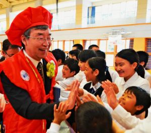児童とハイタッチしながら花道を進む堀越泉校長(左)=名護市・東江小学校