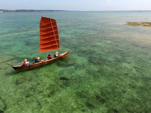 エメラルドグリーン色の海を風を受け進む帆かけサバニ(小型無人機から)
