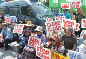 新基地建設に伴う護岸着工に抗議し、プラカードを掲げて座り込む市民=25日午前10時すぎ、名護市辺野古