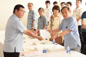 仲間一金武町長(左)から要請書を受け取る菅義偉官房長官=19日、名護市・ホテルゆがふいんおきなわ