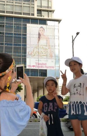 安室奈美恵さんの巨大ポスターをバックに記念撮影する人たち=9日、那覇市久茂地・タイムスビルイムスビル(古謝克公撮影)