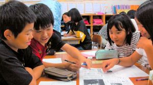 「沖縄全戦没者追悼式」を報じる全国紙の1面を読む児童たち=3日、沖縄市立比屋根小学校