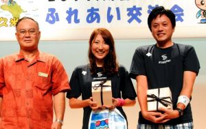 台風で大会中止となっても開かれた「2017久米島マラソンふれあい交流会」で、大田治雄久米島町長(左)から祝福を受ける久米和也さん、絢子さん夫妻=10月21日、久米島町具志川農村環境改善センター