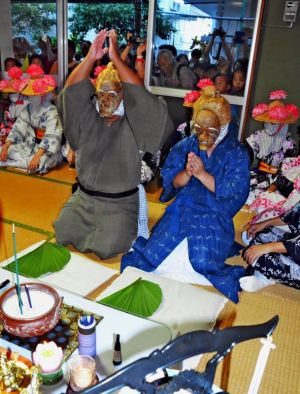 多くの見物客が見守る中、訪問先の仏壇に手を合わせるウシュマイ(左)とンミー=15日、石垣市登野城