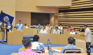 自粛要請無視に関する抗議決議の審議で、提案した自民党会派の議員たち(左)に質問する古堅茂治氏(右)=15日、那覇市議会