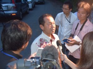 流弾事件の一報を聞き現場付近を訪ね、報道陣の取材に答える渡具知武豊名護市長=21日午後7時35分、名護市数久田