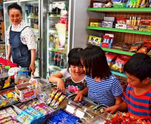 子どもたちのお菓子選びを見守る本永佳子さん(左)=12日、宜野湾市宇地泊の駄菓子屋よっちゃんの店