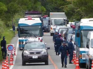 (資料写真)前後を挟む警察車両と、道路脇に立った機動隊員に守られながら砂利を運ぶ工事用トラック=2016年7月26日、東村高江