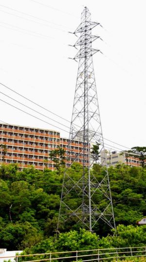 高さ制限超過で移設が決まった沖縄電力の送電鉄塔。約80メートルの距離にある沖縄高専の学生寮(後方)は適用除外とされた=名護市辺野古