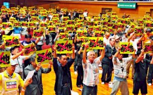 陸自配備に反対するプラカードを掲げ、中山義隆市長の受け入れ表明に抗議する市民ら=29日、石垣市総合体育館