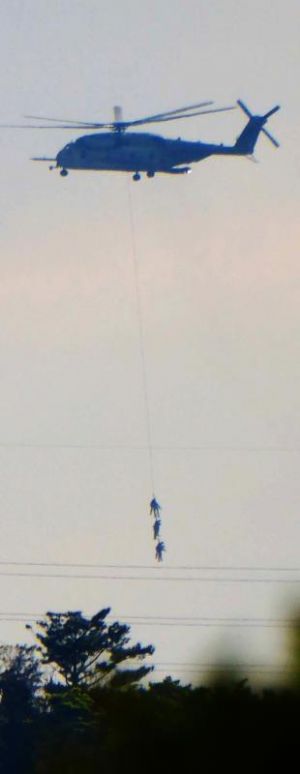 兵士3人をつり下げ、飛行訓練するCH53Eヘリコプター=4日、名護市の上空