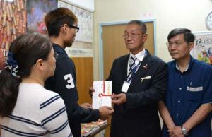 鄭さん(左から2人目)に支援金を手渡す琉球華僑総会の張本光輝会長(同3人目)と台北駐日経済文化代表処那覇分処の蘇啓誠処長(右)=19日、那覇市・琉球華僑総会