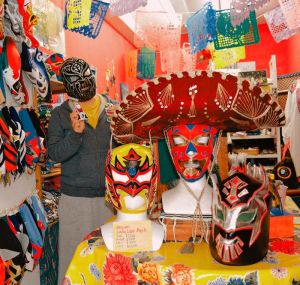 ルチャリブレのマスクや工芸品が並ぶ店内。普段は素顔で接客する与儀静香さんも「顔が新聞に出るといろいろ大変」とマスクをかぶった=那覇市牧志