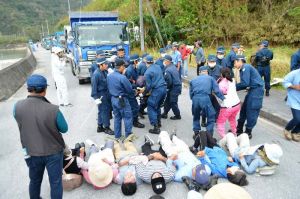 ダンプカーによる石材運搬を阻止しようと路上に寝転がり、機動隊員に排除される市民=13日午前9時すぎ、国頭村・奥港