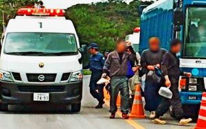 警察車両(左)から降り、米軍北部訓練場に入る作業員ら=2日午後0時ごろ、東村高江のN1ゲート(読者提供、画像の一部を加工しています)