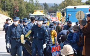 国道に並ぶミキサー車などの基地内進入のため、新基地建設に反対する市民らを排除する県警機動隊員ら=14日正午ごろ、名護市辺野古の米軍キャンプ・シュワブゲート前
