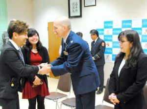 救助したジョン・コットンさん(左から3人目)と金城菜未さん(同4人目)に握手する、けがをした女性の家族ら=1日、嘉手納町・ニライ消防本部