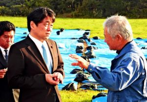 米軍ヘリ炎上事故の現場で被害者の西銘晃さん(右)から話を聞く小野寺五典防衛相=25日午前、東村高江