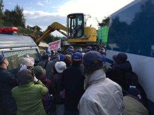 新基地建設に反対する市民らの横を通り、米軍キャンプ・シュワブ内に入る工事車両=27日午前、名護市辺野古