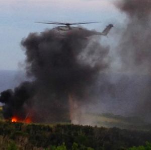 墜落直後の現場。黒煙をあげている米軍機「CH53E」(左下)の消火活動にあたるヘリ(中央)=11日午後6時9分、東村高江(西銘美恵子さん提供)