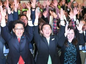 2期目の当選確実を決め支持者らとバンザイする松本哲治氏(中央)=12日午後9時35分、浦添市屋富祖の選対事務所