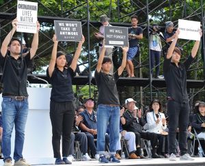 県民大会の壇上でメッセージボードを掲げる元山仁士郎さん(左)、眞鍋詩苑さん(左から3人目)、小波津義嵩さん(右)=2016年6月19日、那覇市・奥武山公園陸上競技場