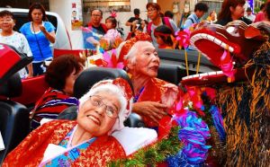 家族や地域住民に祝福され、カジマヤーパレードを楽しむ金城トミさん(手前)と福地千代さん=17日、那覇市若狭(喜屋武綾菜撮影)